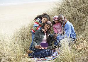 Family Sitting In Dunes Enjoying Picnic On Winter Beach