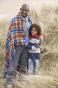 Father And Son Wrapped In Blanket Amongst Dunes On Winter Beach