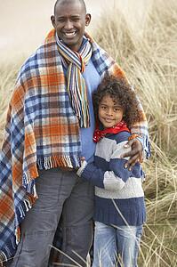Father And Son Wrapped In Blanket Amongst Dunes On Winter Beach