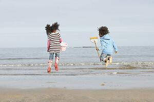 Two Children Playing By Sea On Winter Beach