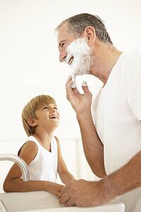 Grandson Watching Grandfather Shaving In Bathroom Mirror