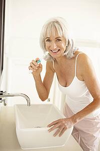 Senior Woman Brushing Teeth In Bathroom