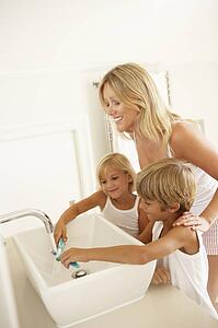 Mother And Children Brushing Teeth In Bathroom Together