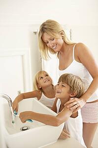 Mother And Children Brushing Teeth In Bathroom Together