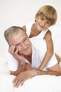 Grandfather Relaxing On Bed With Grandson