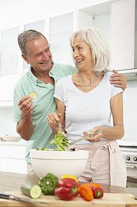 Senior Couple Preparing Salad In Modern Kitchen