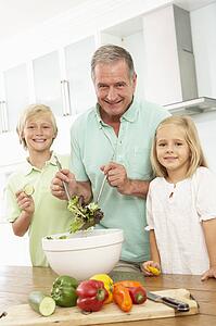 Grandchildren Helping Grandfather To Prepare Salad In Modern Kitchen