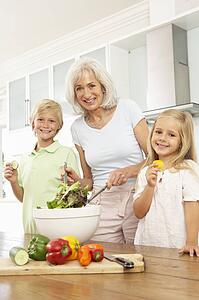 Grandchildren Helping Grandmother To Prepare Salad In Modern Kitchen