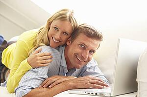 Couple Using Laptop Relaxing Sitting On Sofa At Home