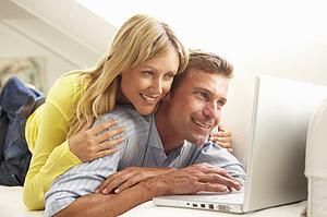 Couple Using Laptop Relaxing Sitting On Sofa At Home
