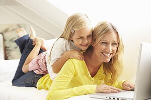 Mother And Daughter Using Laptop Relaxing Sitting On Sofa At Home