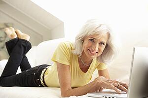 Senior Woman Using Laptop Relaxing Sitting On Sofa At Home