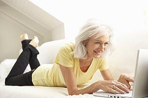 Senior Woman Using Laptop Relaxing Sitting On Sofa At Home