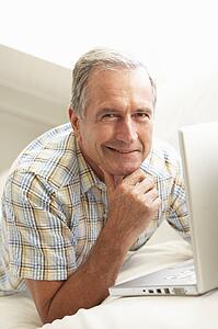 Senior Man Using Laptop Relaxing Sitting On Sofa At Home