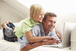 Father And Son Using Laptop Relaxing Sitting On Sofa At Home