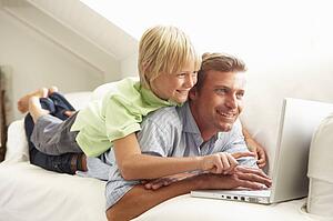 Father And Son Using Laptop Relaxing Sitting On Sofa At Home