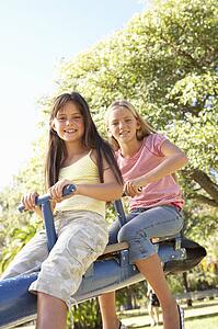 Two Girls Riding On See Saw In Playground