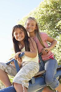 Two Girls Riding On See Saw In Playground