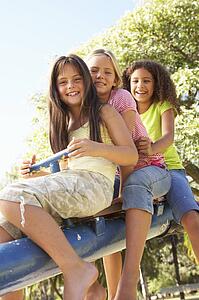 Three Girls Riding On See Saw In Playground