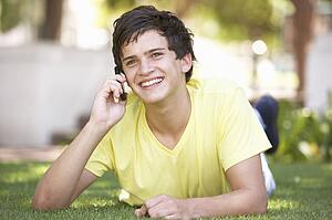 Teenage Boy Laying In Park Using Mobile Phone