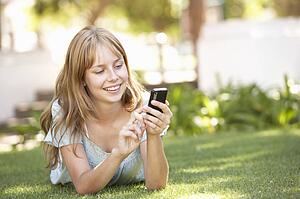 Teenage Girl Laying In Park Using Mobile Phone