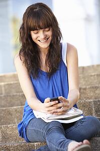 Teenage Student Sitting Outside On College Steps Using Mobile Phone