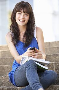 Teenage Student Sitting Outside On College Steps Using Mobile Phone