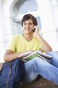 Male Teenage Student Sitting Outside On College Steps Using Mobile Phone
