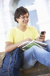 Male Teenage Student Sitting Outside On College Steps Using Mobile Phone