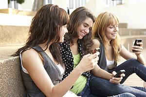 Group Of Teenage Students Sitting Outside On College Steps Using Mobile Phone