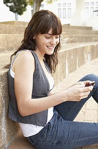 Teenage Student Sitting Outside On College Steps Using Mobile Phone