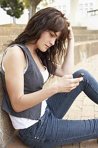 Unhappy Female Teenage Student Sitting Outside On College Steps Using Mobile Phone