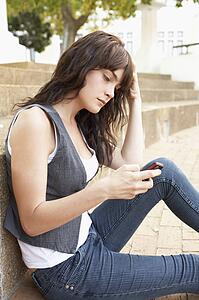Unhappy Female Teenage Student Sitting Outside On College Steps Using Mobile Phone