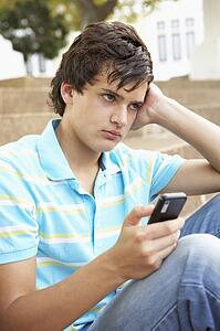 Unhappy Male Teenage Student Sitting Outside On College Steps Using Mobile Phone