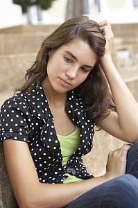 Unhappy Female Teenage Student Sitting Outside On College Steps Using Mobile Phone
