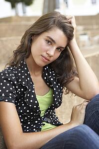 Unhappy Female Teenage Student Sitting Outside On College Steps Using Mobile Phone