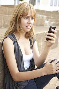 Unhappy Female Teenage Student Sitting Outside On College Steps Using Mobile Phone
