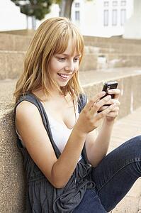 Unhappy Female Teenage Student Sitting Outside On College Steps Using Mobile Phone