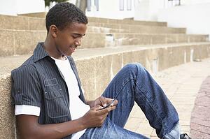 Male Teenage Student Sitting Outside On College Steps Using Mobile Phone