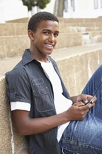 Male Teenage Student Sitting Outside On College Steps Using Mobile Phone