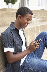 Male Teenage Student Sitting Outside On College Steps Using Mobile Phone