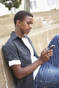 Unhappy Male Teenage Student Sitting Outside On College Steps Using Mobile Phone