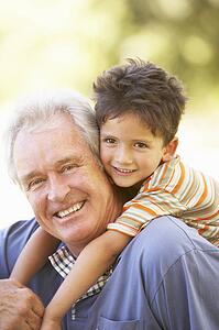Grandfather Giving Grandson Ride On Back In Park