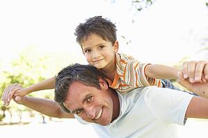 Father Giving Son Ride On Back In Park