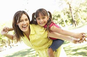 Mother Giving Daughter Ride On Back In Park