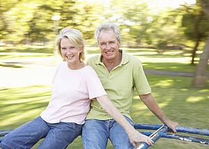 Senior Couple Riding On Roundabout In Park