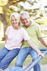 Senior Couple Riding On Roundabout In Park