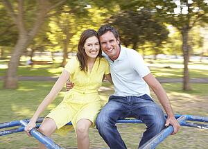 Young Couple Riding On Roundabout In Park