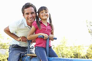 Father And Daughter Riding On See Saw In Playground