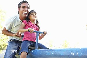 Father And Daughter Riding On See Saw In Playground